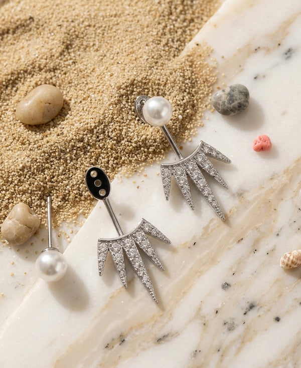 Silver earrings with pearls on a textured surface resembling sand and stone.