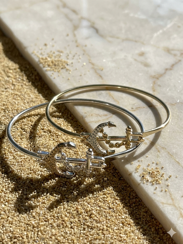 Gold and silver bangles with anchor designs on a marble surface.