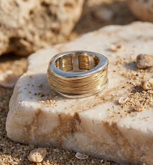 Gold ring on a textured stone surface with sand and shells around