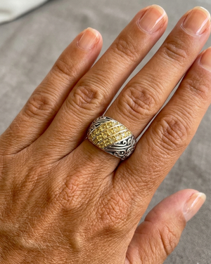 Close-up of a hand wearing a silver ring with a yellow gemstone on a gray background