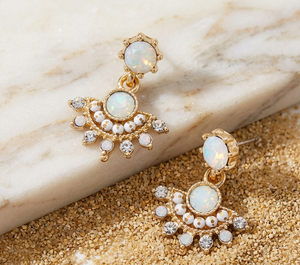Gold earrings with opal stones on a marble and sand background