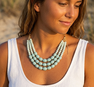 Woman wearing a light blue beaded necklace on a beach