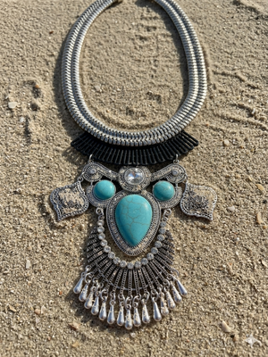 Decorative necklace with turquoise stones and silver accents on a sandy surface