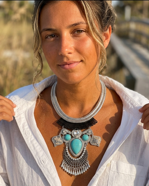 Woman wearing a large, ornate necklace with turquoise stones outdoors.