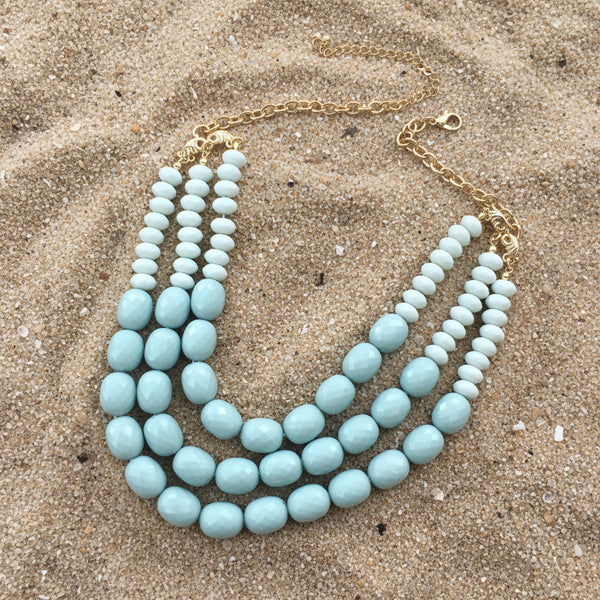Turquoise beaded necklace with gold chain on a light pink background