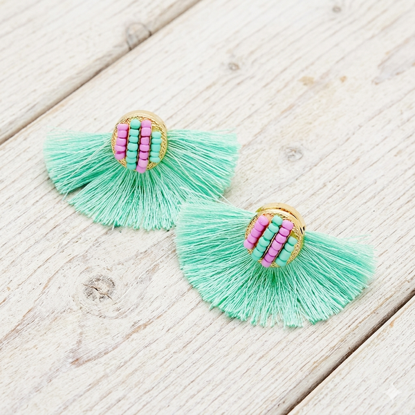 Turquoise tassel earrings with pink and gold center on a wooden surface