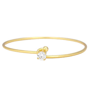 Gold bangle with a heart-shaped diamond on a light gray background