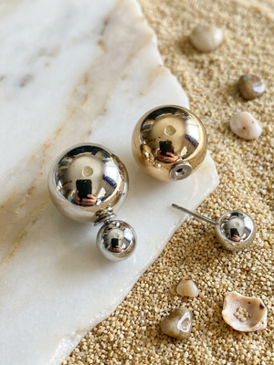 Pair of gold and silver spherical earrings on a textured surface with shells.