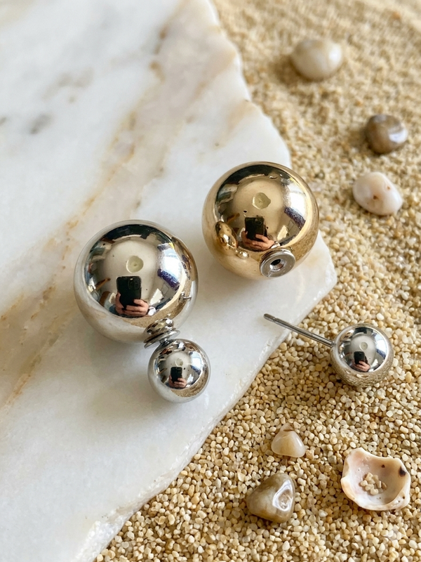 Pair of gold and silver spherical earrings on a textured surface with shells.