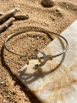 Gold bracelet with anchor design on a stone surface