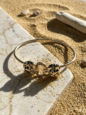 Gold bracelet with black stones on a stone surface with sand and driftwood in the background