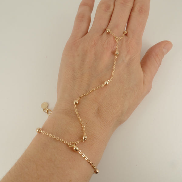 Gold bracelet on a hand against a plain background