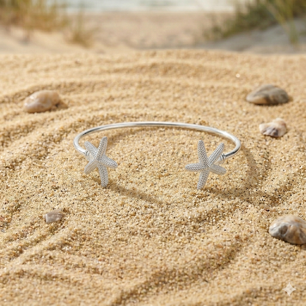 Silver bracelet with starfish designs on a sandy surface