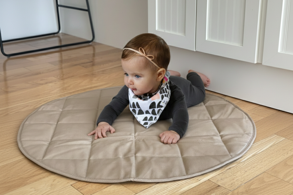 Baby lying on a round beige mat in a kitchen