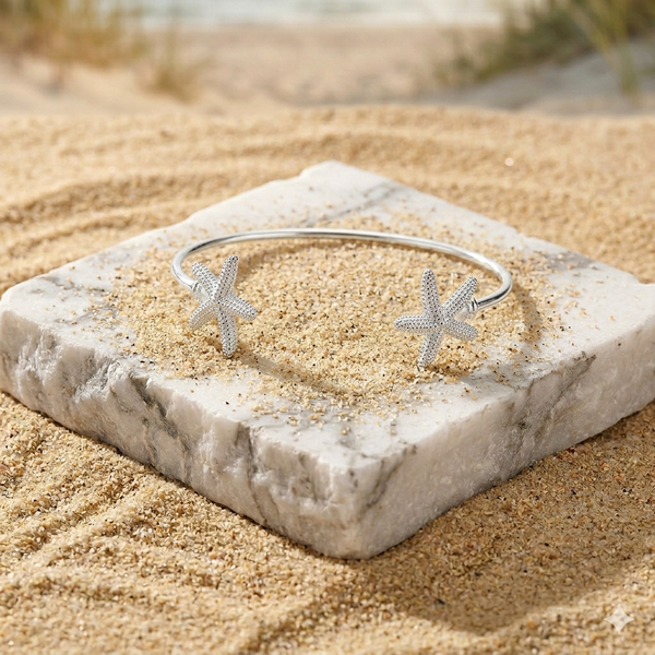 Silver bracelet with starfish designs on a stone block in a sandy setting