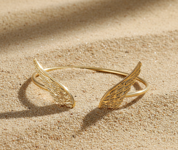 Gold wing-shaped bracelet on a sandy surface