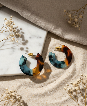 Tortoiseshell hoop earrings on a marble surface with dried flowers.