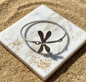 Silver bracelet with dragonfly design on a marble coaster with sand around