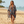 Charger l'image dans la galerie, A woman walking on a sandy beach wearing a sheer, open-front patterned cover-up with tassels over denim shorts. The cover-up features a geometric design in navy blue, beige, brown, and light blue.
