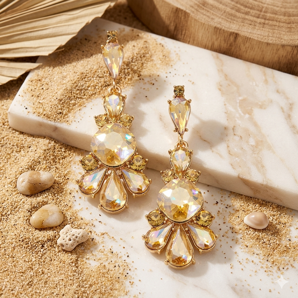 Gold earrings with clear stones on a sandy surface