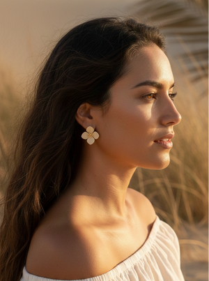 Woman in a white off-shoulder top standing in a desert-like setting with sand and palm leaves.