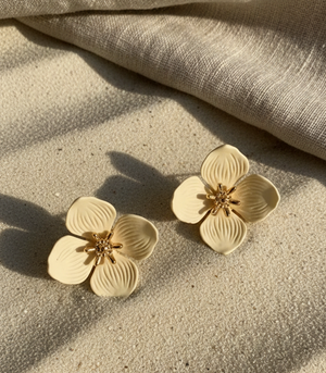 Gold flower-shaped earrings on a textured beige surface