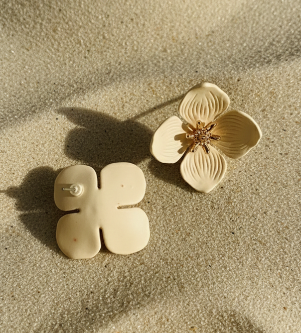 Gold floral and geometric earrings on sand