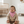 Load image into Gallery viewer, Child wearing a beige sweater and pink bib sitting on a white carpet in a nursery.
