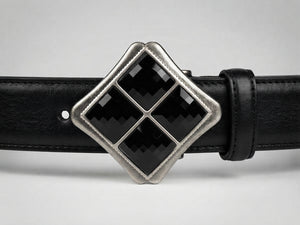 A close-up of a black leather belt featuring a large diamond-shaped silver buckle with four black inlay panels.