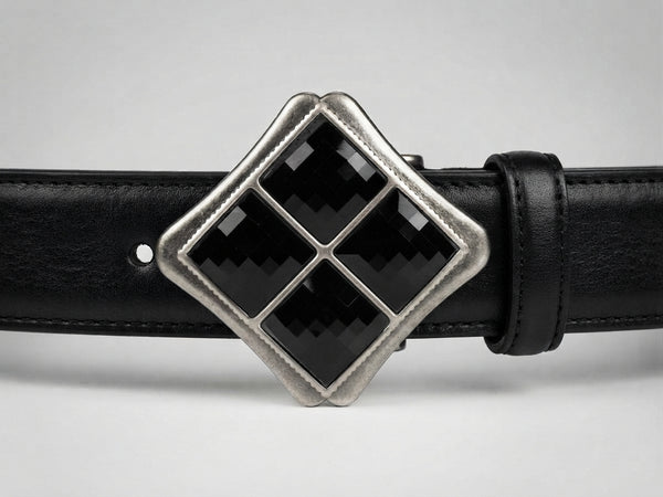 A close-up of a black leather belt featuring a large diamond-shaped silver buckle with four black inlay panels.
