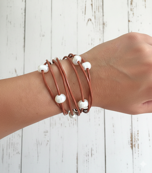 Wrist wearing multiple brown bracelets with white beads on a light wooden background