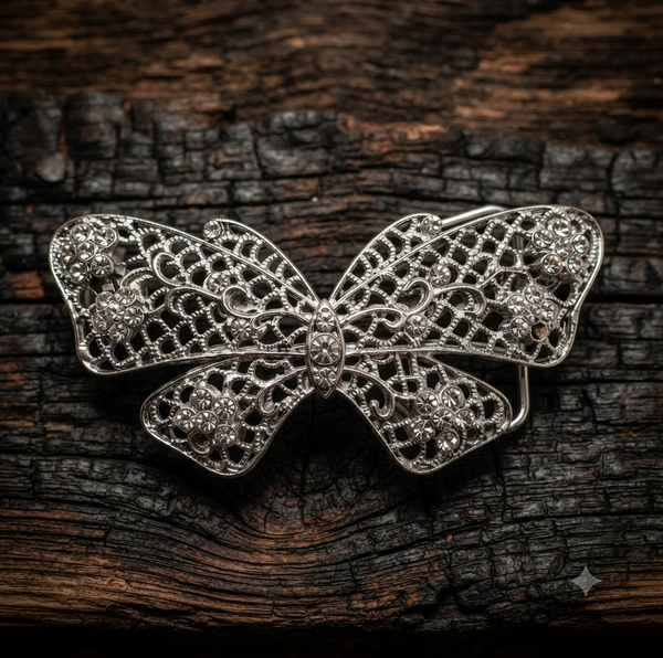 A silver butterfly-shaped filigree brooch with floral wire details, displayed on a dark, textured wooden surface.