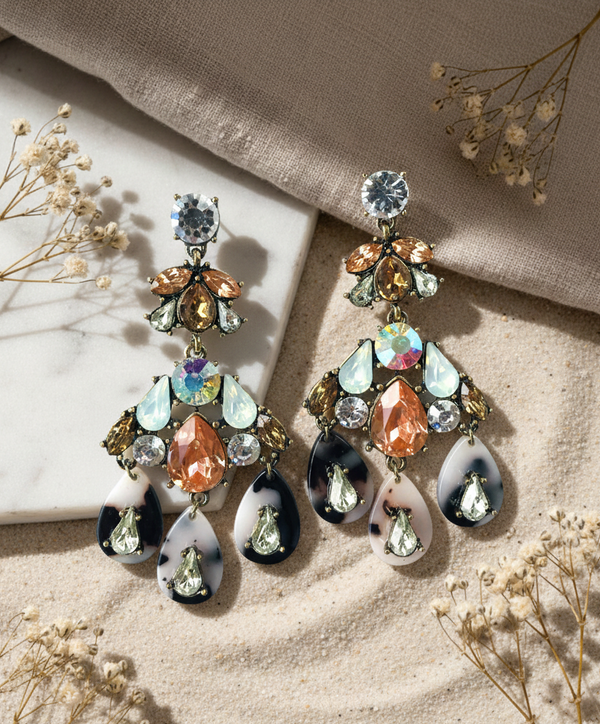 Multicolored gemstone earrings on a beige fabric background with dried flowers.