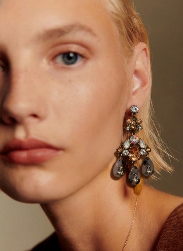 Close-up of a woman wearing a pair of ornate earrings with a neutral background