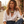 Charger l'image dans la galerie, A woman wearing a white button-down shirt and blue jeans sits outdoors, wearing a chunky statement necklace with yellow, blue, and white beads and silver-toned charms.

