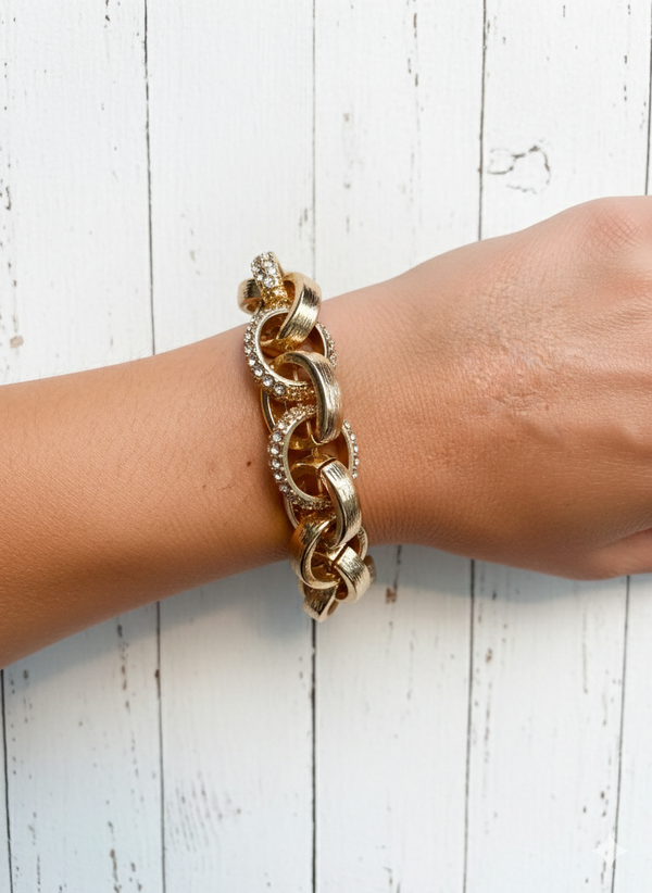 Gold chain bracelet on a wrist against a white wooden background