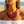 Charger l'image dans la galerie, A close-up lifestyle shot of a woman on a beach wearing a chunky statement necklace. The necklace features large, layered translucent red disc elements woven with red beads and accented with small silver beads.
