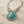 Charger l'image dans la galerie, A silver filigree statement necklace featuring a large oval turquoise stone surrounded by clear rhinestones, displayed on a rustic light wood surface.
