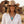 Charger l'image dans la galerie, A smiling woman wearing a tan cowboy hat, white button-up shirt, and layered silver necklaces with a large turquoise pendant, photographed outdoors against a blurred rustic wooden building.
