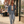Charger l'image dans la galerie, A woman walking on a city sidewalk wearing a light-wash blue denim jacket over a cream crop top, matching light-wash jeans, and white sneakers, with a brown shoulder bag.
