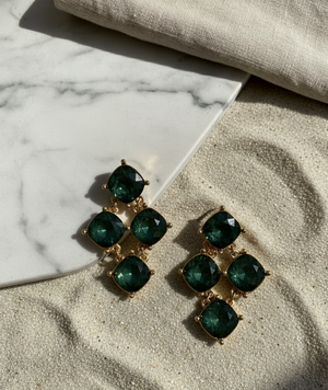Green gemstone earrings on a marble surface with sand