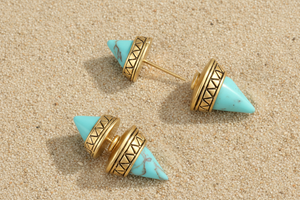 Turquoise and gold earrings on a sandy background