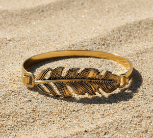 Gold feather bracelet on a sandy surface