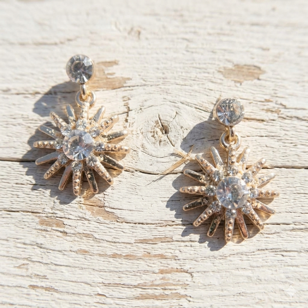 Gold sunburst earrings with clear gemstones on a wooden surface