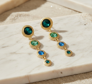 Gold earrings with green gemstones on a marble surface