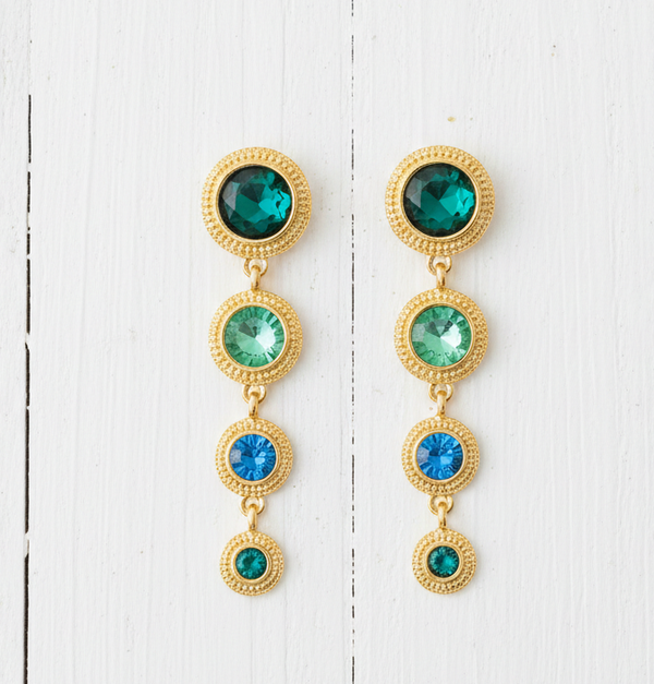 Gold earrings with green and blue gemstones on a white wooden background