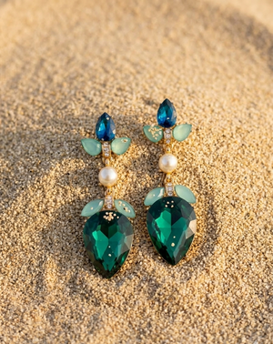 Green teardrop earrings with pearl and gemstone details on a sandy background