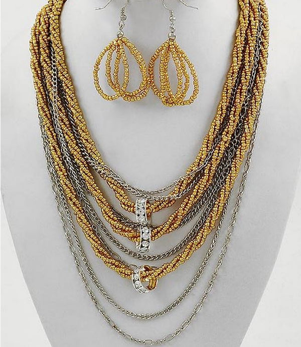 A multi-layered statement necklace set with matching teardrop-shaped dangle earrings, displayed on a white mannequin bust. The necklace features multiple strands of small gold and silver beads, silver chain layers, and a central silver-toned pavé charm.