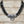 Load image into Gallery viewer, A multi-strand black beaded necklace with a polished silver-toned central clasp and hanging ring, displayed on a light wood plank background.
