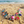 Load image into Gallery viewer, A colorful beaded necklace with square and round glass beads in pink, blue, green, purple, orange, and brown, displayed on a sandy beach with the ocean in the background.
